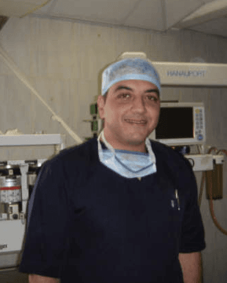 Mr Sherif Elshazly in surgical scrubs and a theatre cap, standing in an operating theatre