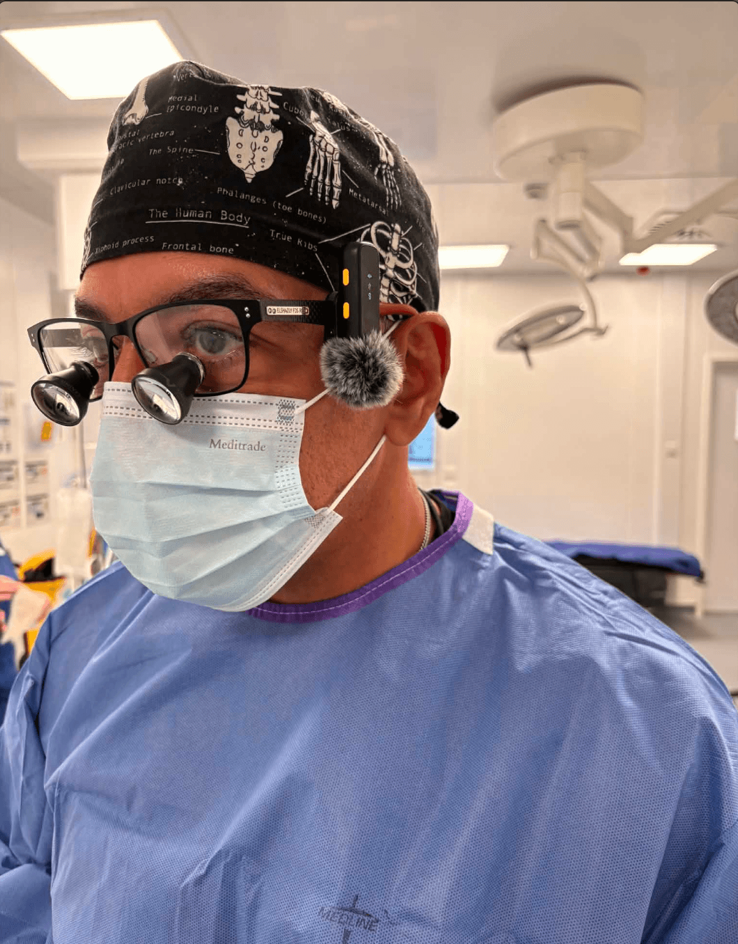 Mr Sherif Elshazly in an operating theatre, in surgical gown, mask, loupes and headlight