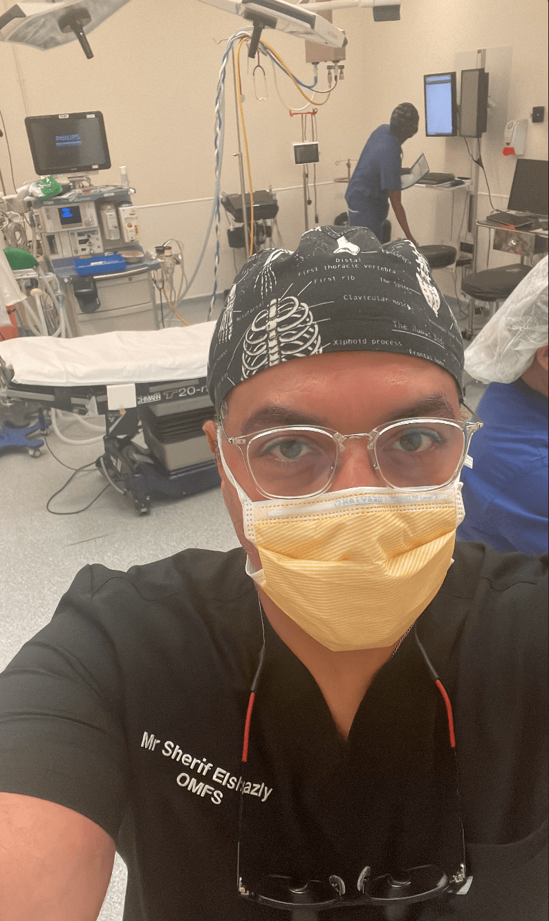 Mr Sherif Elshazly in an operating theatre, scrub top embroidered "Mr Sherif Elshazly / OMFS"